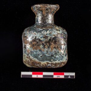 The same bottle, viewed from the side, post-conservation. The glass is visible and significant degradation is apparent.