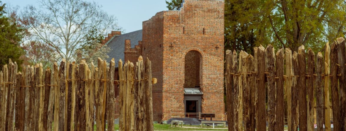 The 17th-century brick church tower is viewed through the pathway of the wooden palisade on a sunny day