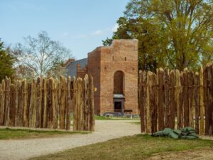 The 17th-century brick church tower is viewed through the pathway of the wooden palisade on a sunny day