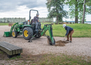 Site Supervisor Anna Shackeford (on the backhoe) and Staff Archaeologist Caitlin Delmas test the depth of the gravel walkway to prepare for the installation of new aggregate.