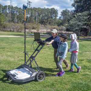 Staff Archaeologist Ren Willis conducts a GPR survey of the grounds north of the Church Tower and explains the process to some visitors. Ren is using a GPR machine brought by Dr. David Leslie of TerraSearch Geophysical.