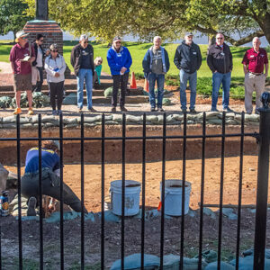 Staff Archaeologist Caitlin Delmas gives an archaeology update to volunteers and staff just outside the Archaearium as Staff Archaeologist Ren Willis conducts excavations there.