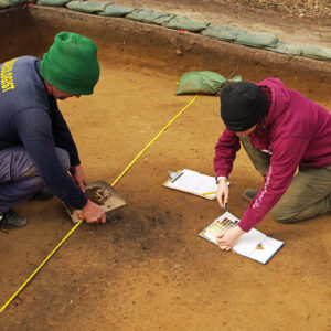 Staff Archaeologist Gabriel Brown and Archaeological Field Technician Ren Willis at the excavations near the Godspeed Cottage. Ren is using a Munsell color chart to classify a soil sample taken from a burn feature.